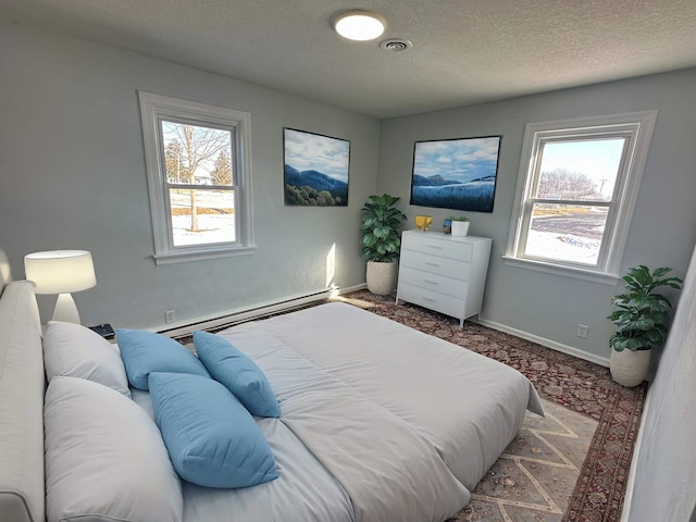 bedroom featuring multiple windows, a baseboard heating unit, and a textured ceiling