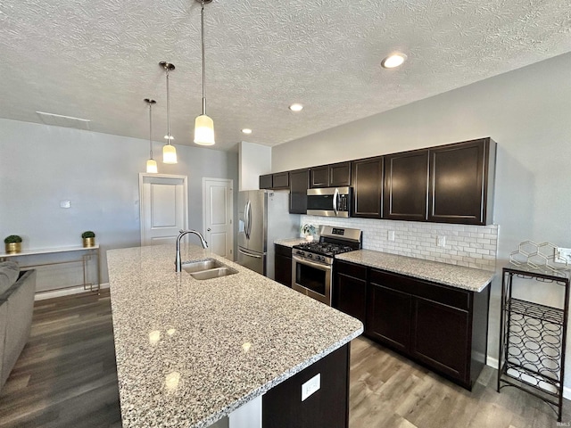 kitchen featuring stainless steel appliances, decorative light fixtures, a kitchen island with sink, and sink