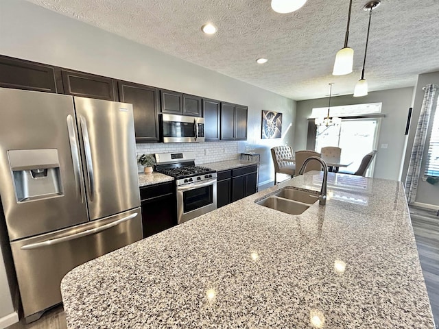 kitchen with light stone counters, appliances with stainless steel finishes, sink, and hanging light fixtures