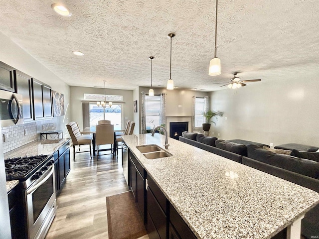 kitchen with pendant lighting, sink, appliances with stainless steel finishes, a kitchen island with sink, and light stone countertops