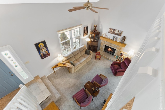 living room with ceiling fan, a towering ceiling, and a stone fireplace