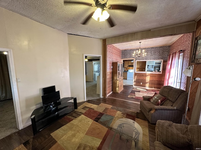 living room featuring brick wall, dark wood-type flooring, ceiling fan with notable chandelier, and a textured ceiling