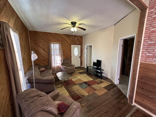 living room with ceiling fan, dark wood-type flooring, a textured ceiling, and wood walls