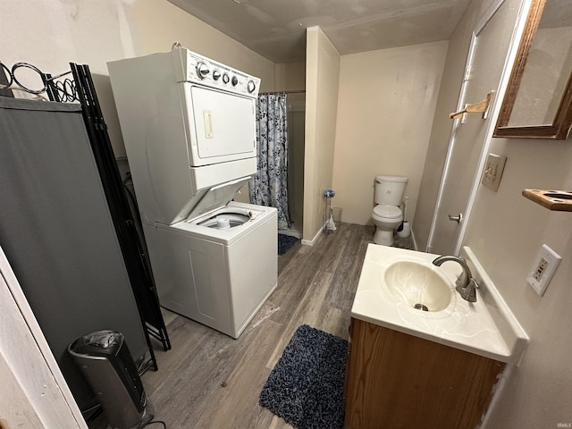 bathroom featuring a shower with shower curtain, vanity, stacked washer / dryer, wood-type flooring, and toilet