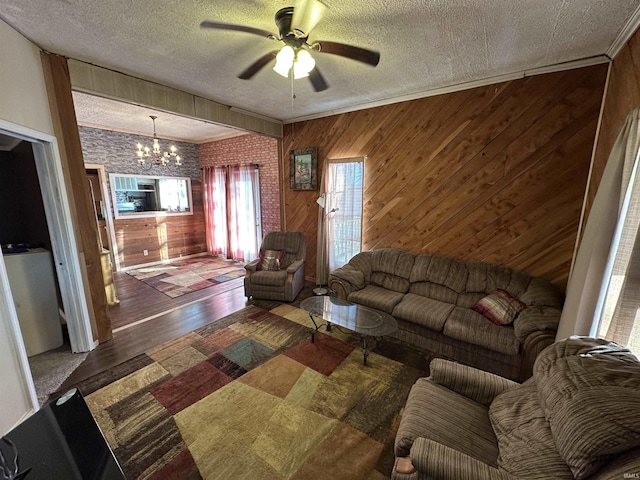 unfurnished living room featuring wood-type flooring, ceiling fan with notable chandelier, a textured ceiling, and wooden walls