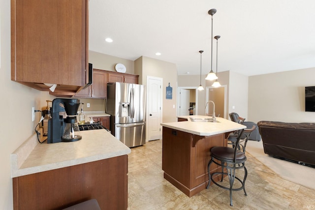 kitchen with sink, a breakfast bar area, a kitchen island with sink, stainless steel refrigerator with ice dispenser, and decorative light fixtures