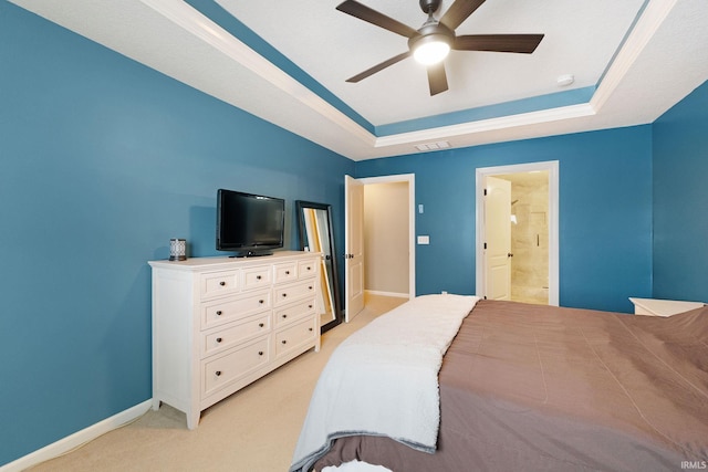 carpeted bedroom with a raised ceiling, connected bathroom, and ceiling fan