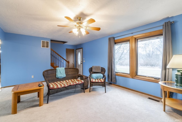 living area featuring ceiling fan, light carpet, and a textured ceiling