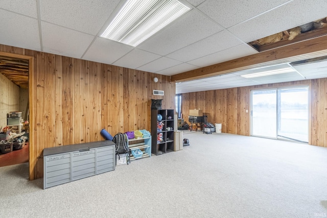 basement with carpet flooring, a paneled ceiling, and wood walls