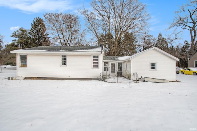 snow covered rear of property featuring a sunroom