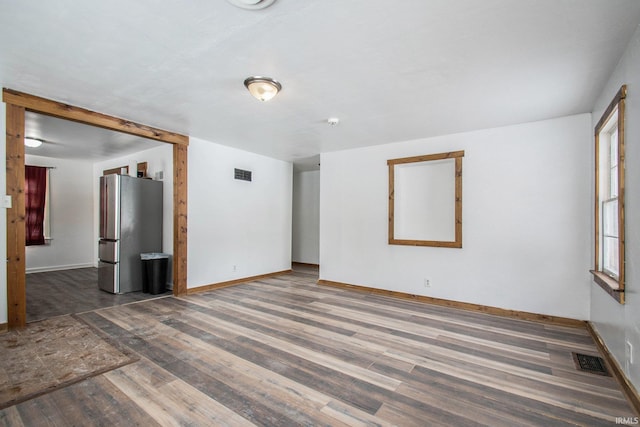 empty room with wood finished floors, visible vents, and baseboards