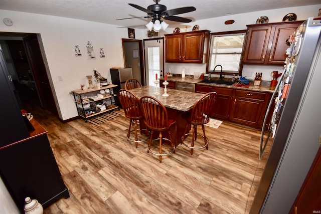 kitchen with sink, light stone counters, light wood-type flooring, a kitchen breakfast bar, and a kitchen island