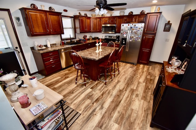 kitchen featuring sink, stainless steel appliances, a center island, light hardwood / wood-style floors, and light stone countertops