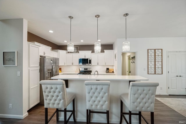 kitchen featuring appliances with stainless steel finishes, light countertops, decorative light fixtures, and an island with sink