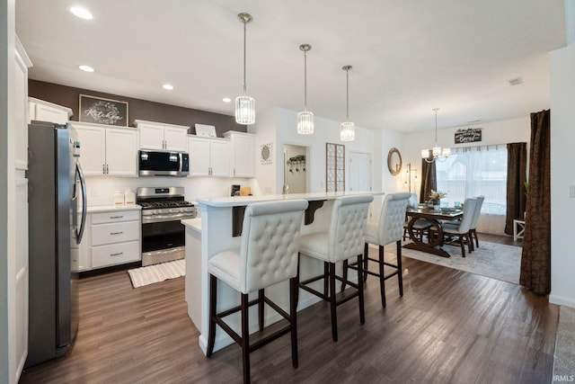 kitchen featuring a center island with sink, white cabinets, hanging light fixtures, stainless steel appliances, and light countertops