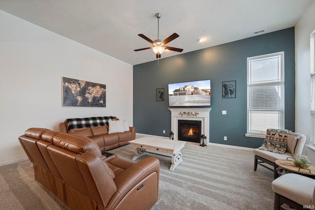 living room with visible vents, a ceiling fan, a glass covered fireplace, light carpet, and baseboards