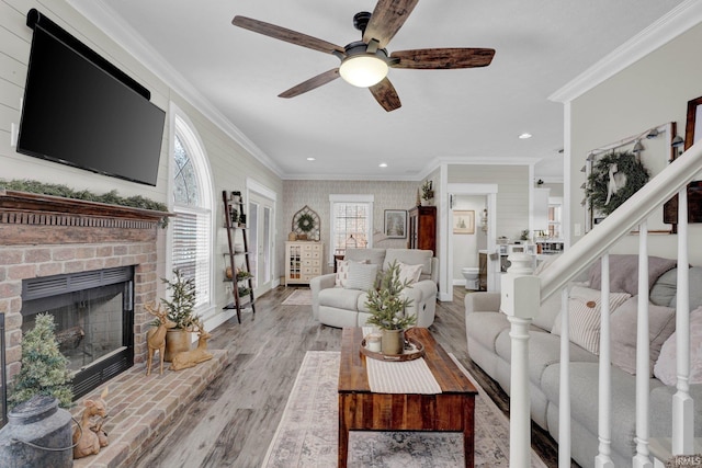 living room featuring crown molding, ceiling fan, a fireplace, and light hardwood / wood-style floors