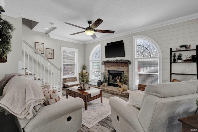 living room with ceiling fan, hardwood / wood-style floors, a fireplace, ornamental molding, and a textured ceiling