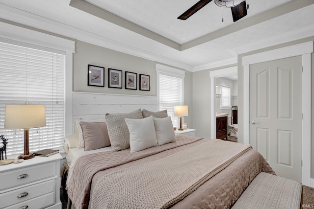 bedroom with a raised ceiling, connected bathroom, and ceiling fan