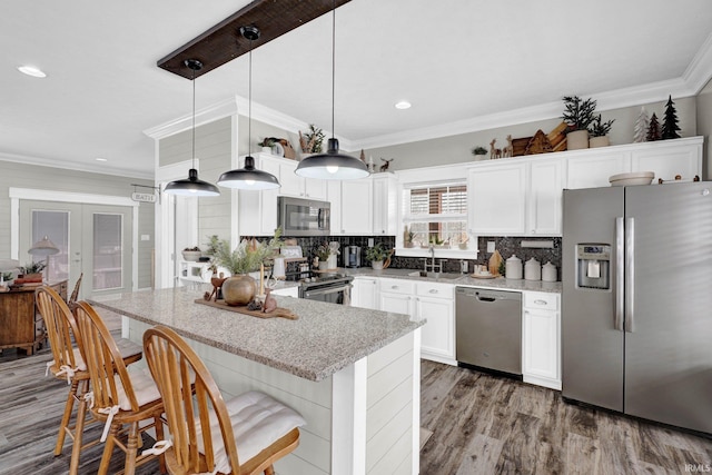 kitchen featuring white cabinetry, appliances with stainless steel finishes, pendant lighting, and crown molding