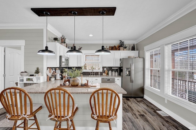 kitchen with stainless steel appliances, ornamental molding, pendant lighting, and white cabinetry