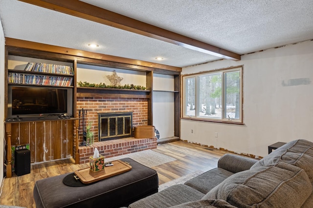 living room featuring beamed ceiling, a fireplace, a textured ceiling, and light wood-type flooring