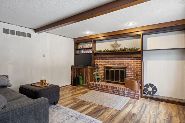 living room with hardwood / wood-style flooring, a brick fireplace, built in features, and a textured ceiling