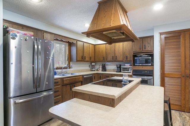 kitchen featuring sink, a center island, a textured ceiling, appliances with stainless steel finishes, and island exhaust hood