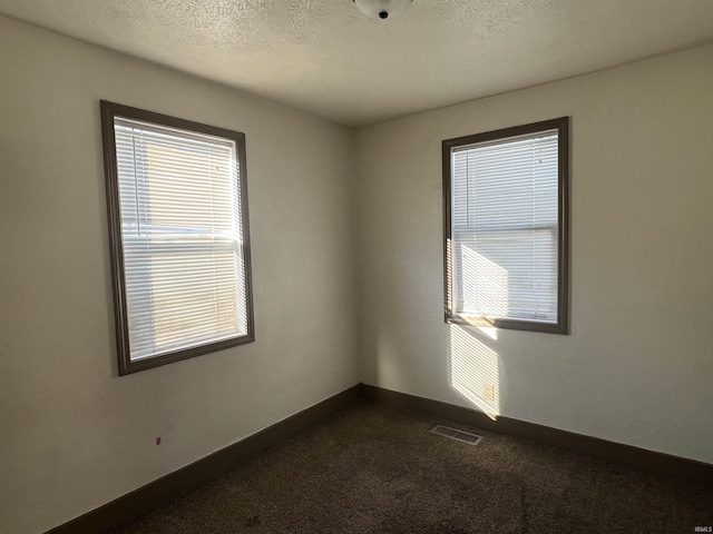 empty room featuring dark carpet and a textured ceiling