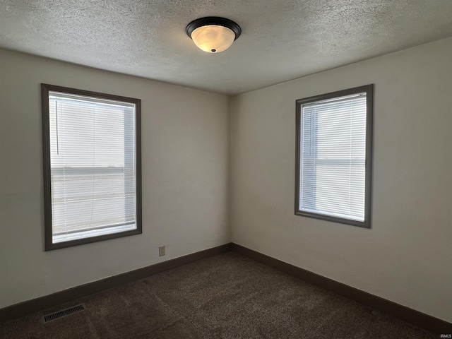 empty room featuring dark colored carpet, a healthy amount of sunlight, and a textured ceiling