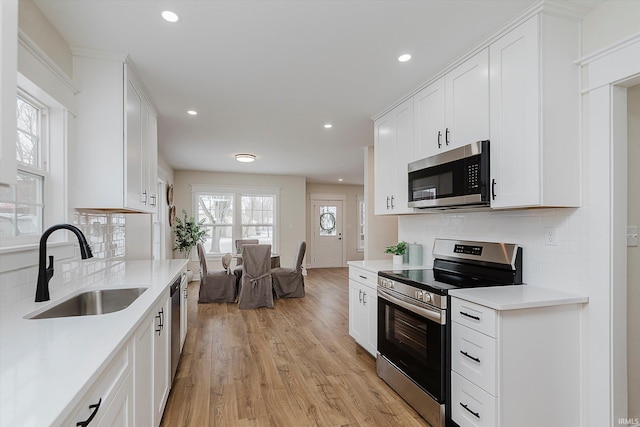 kitchen featuring white cabinetry, sink, backsplash, stainless steel appliances, and light wood-type flooring