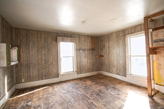 empty room with plenty of natural light, dark wood-type flooring, and wooden walls