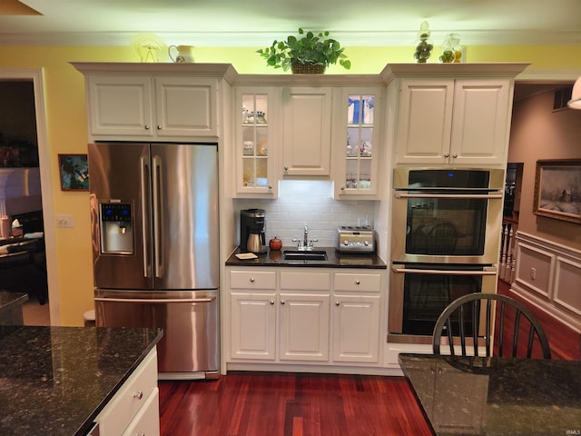 kitchen with ornamental molding, appliances with stainless steel finishes, white cabinets, dark stone counters, and backsplash