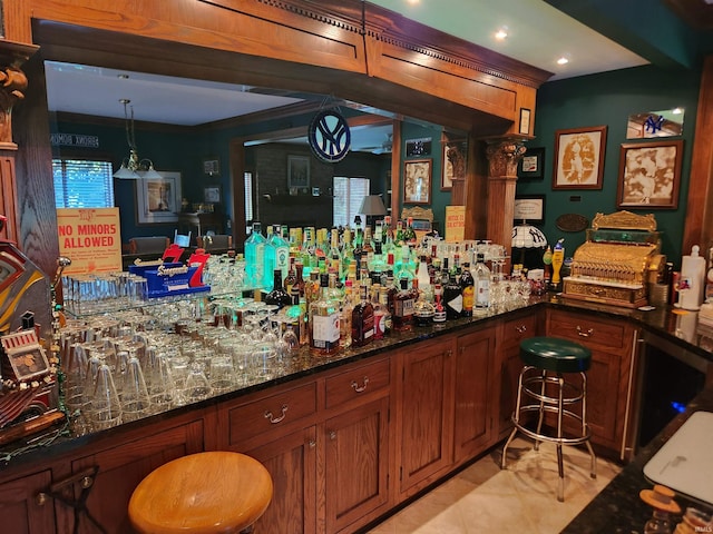 bar with ornamental molding, decorative light fixtures, light tile patterned floors, and dark stone countertops