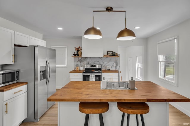 kitchen featuring a kitchen bar, butcher block counters, white cabinetry, hanging light fixtures, and stainless steel appliances