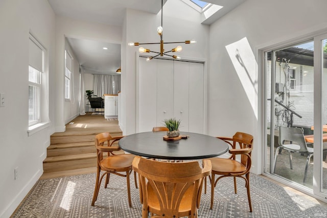 dining area with plenty of natural light, a skylight, light hardwood / wood-style floors, and a notable chandelier