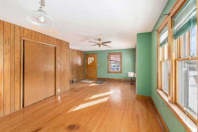 unfurnished living room with ceiling fan, a healthy amount of sunlight, light hardwood / wood-style flooring, and wood walls