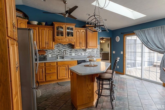 kitchen featuring lofted ceiling with skylight, sink, stainless steel fridge, a kitchen island, and backsplash