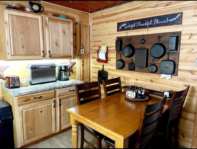 kitchen with light wood-type flooring, wooden walls, light stone countertops, and light brown cabinets