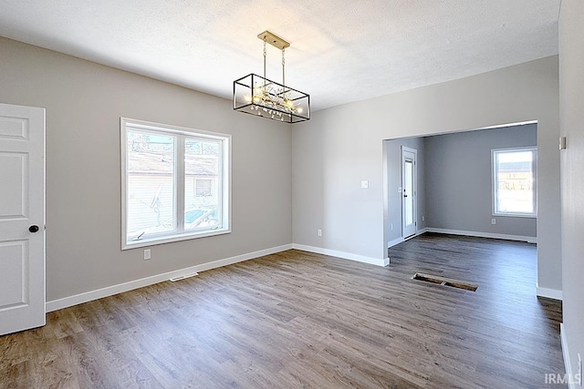 unfurnished dining area with plenty of natural light, hardwood / wood-style floors, a notable chandelier, and a textured ceiling