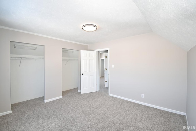 unfurnished bedroom with multiple closets, carpet, lofted ceiling, and a textured ceiling