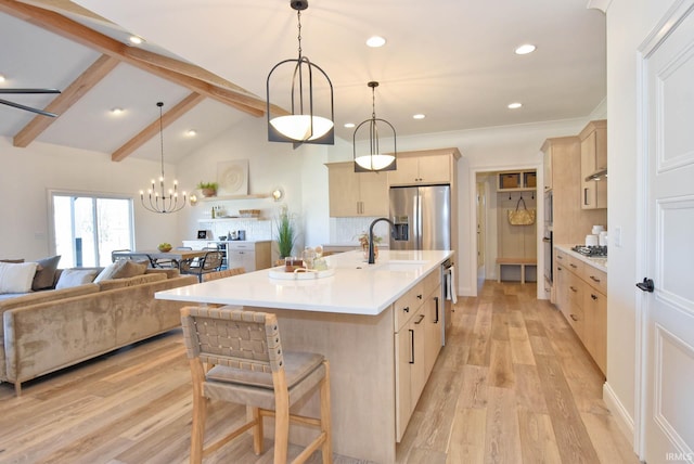 kitchen featuring light brown cabinetry, tasteful backsplash, stainless steel appliances, a center island with sink, and light wood-type flooring