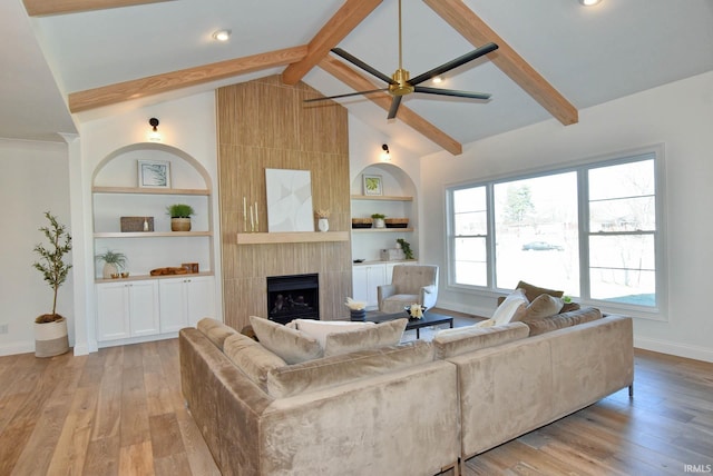 living room featuring lofted ceiling with beams, a large fireplace, light hardwood / wood-style floors, and built in shelves