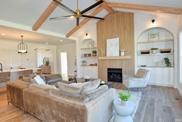 living room with beamed ceiling, a large fireplace, light hardwood / wood-style flooring, and built in shelves