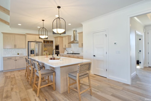 kitchen featuring appliances with stainless steel finishes, tasteful backsplash, light brown cabinets, wall chimney range hood, and a center island with sink