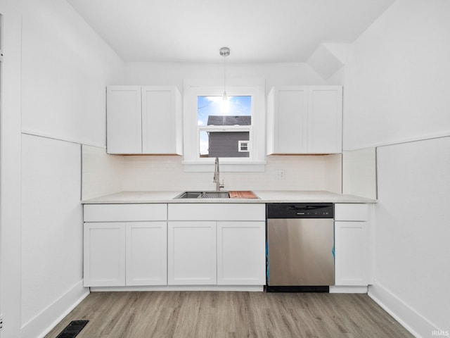 kitchen featuring sink, white cabinets, hanging light fixtures, stainless steel dishwasher, and light hardwood / wood-style flooring