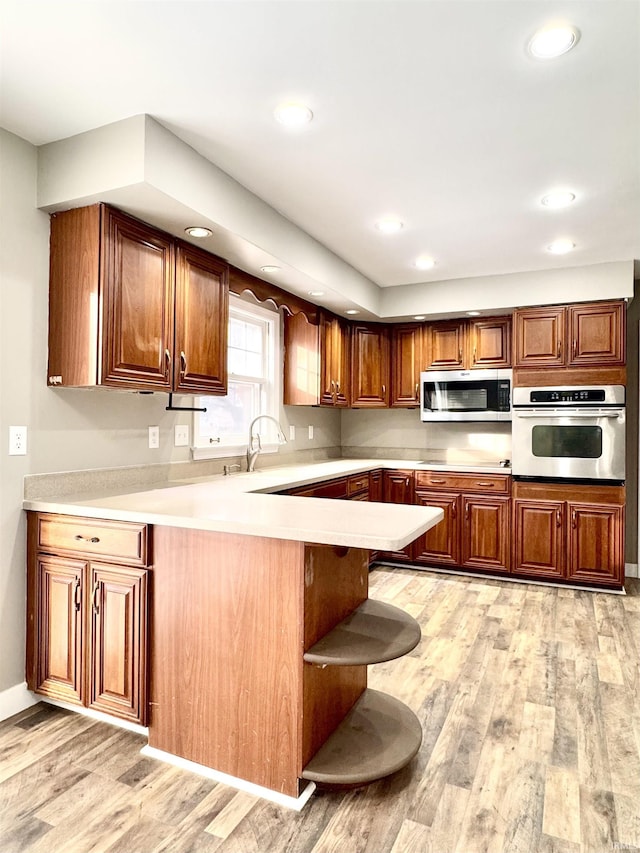 kitchen featuring stainless steel appliances, light countertops, a peninsula, and light wood finished floors