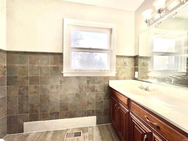 bathroom with a wainscoted wall, visible vents, tile walls, and vanity