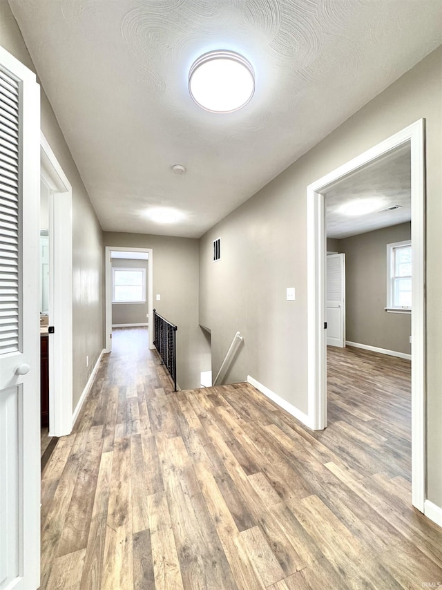 corridor featuring a wealth of natural light, baseboards, an upstairs landing, and wood finished floors