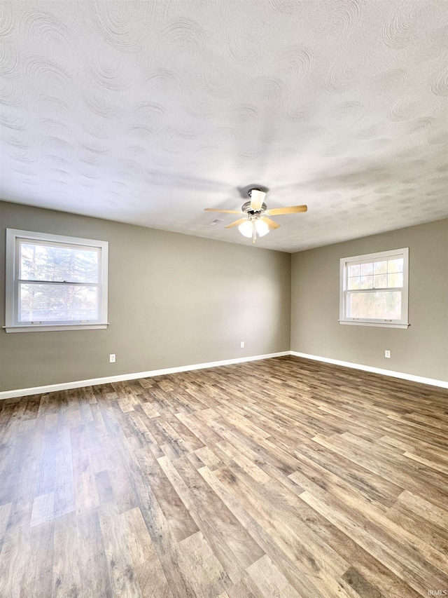 unfurnished room with baseboards, ceiling fan, wood finished floors, and a healthy amount of sunlight